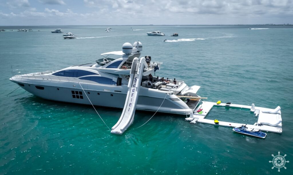 Two luxury yachts are anchored in turquoise water with an inflatable water park and slide