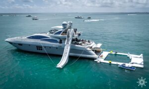 Two luxury yachts are anchored in turquoise water with an inflatable water park and slide